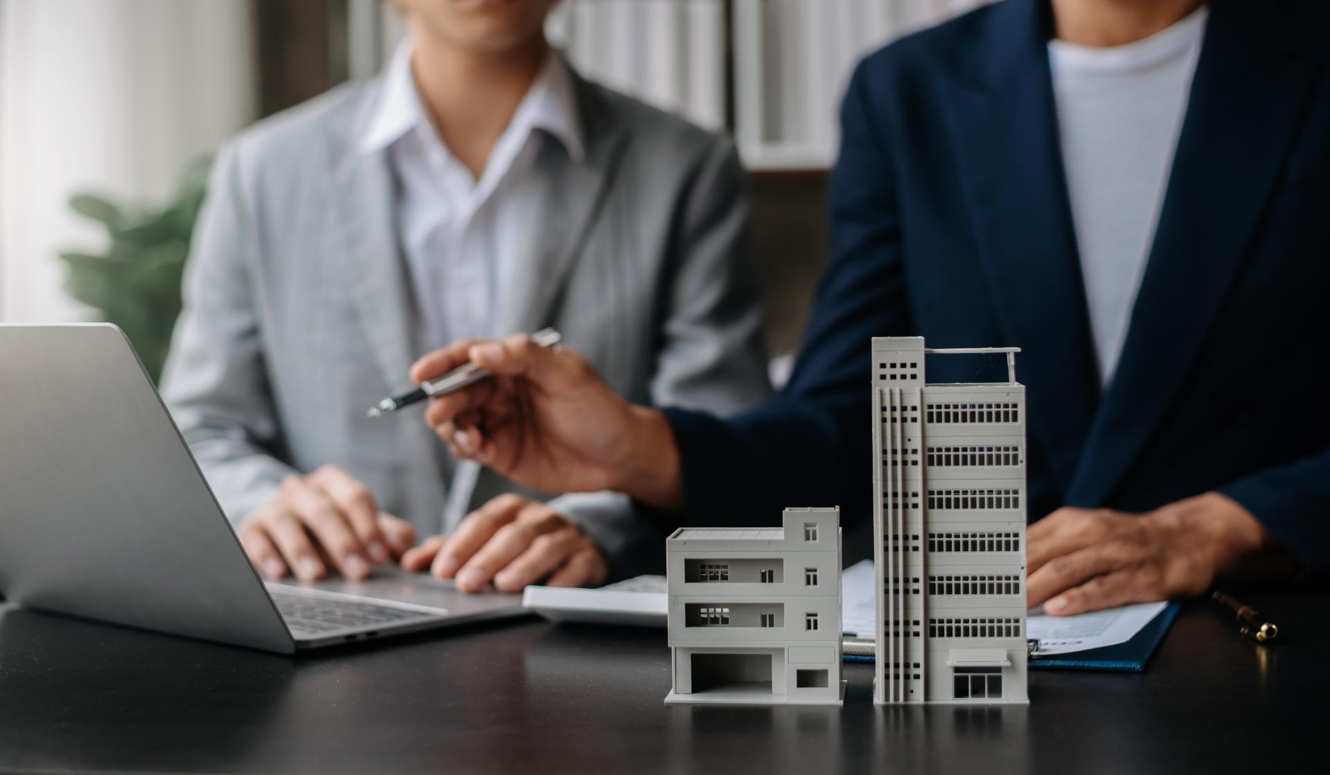 Hombre de traje señala algo en la pantalla de un portátil que está al lado de unas maquetas de edificios